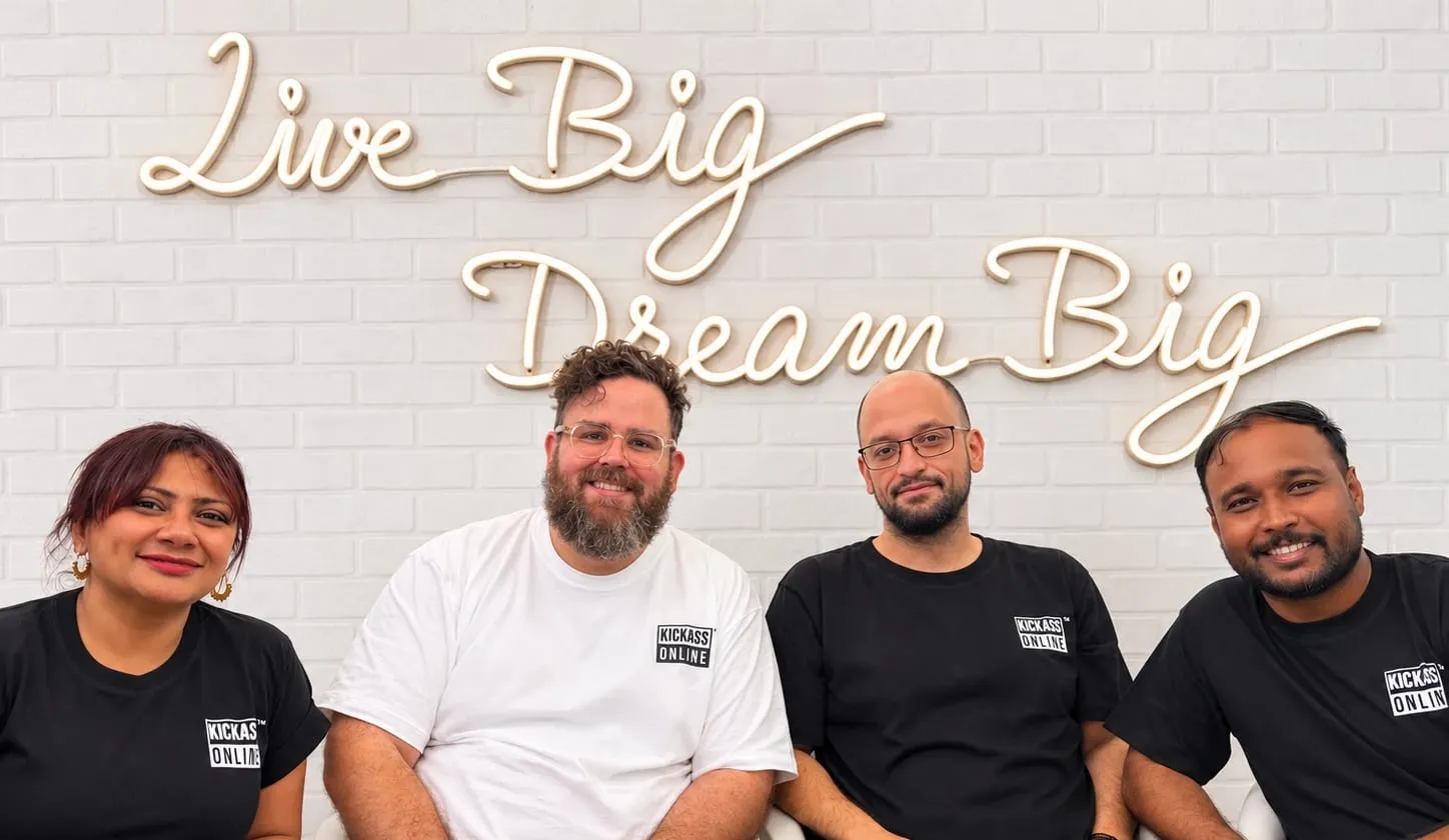 The four of them under neon lettering that reads Live Big, Dream Big