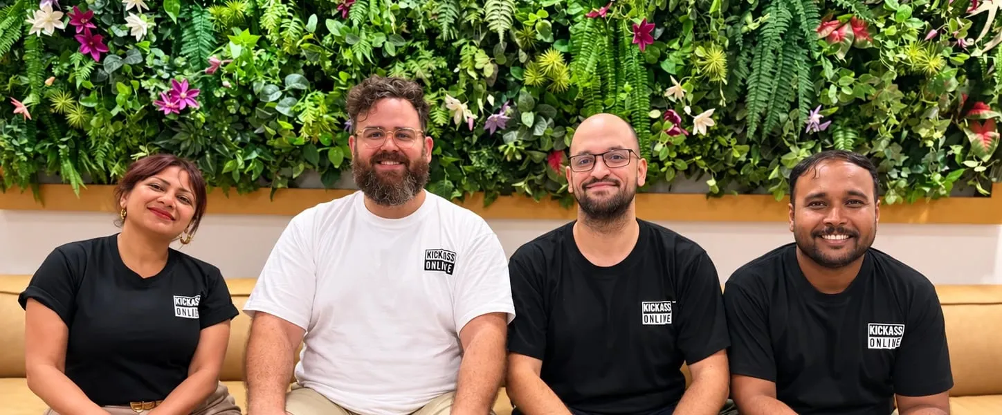 Radhika Dave, Pazbi Zavatzki, Panos Vassos and Linkon Hossain sitting together on a sofa in Kickass Online T-shirts, in front of a living wall
